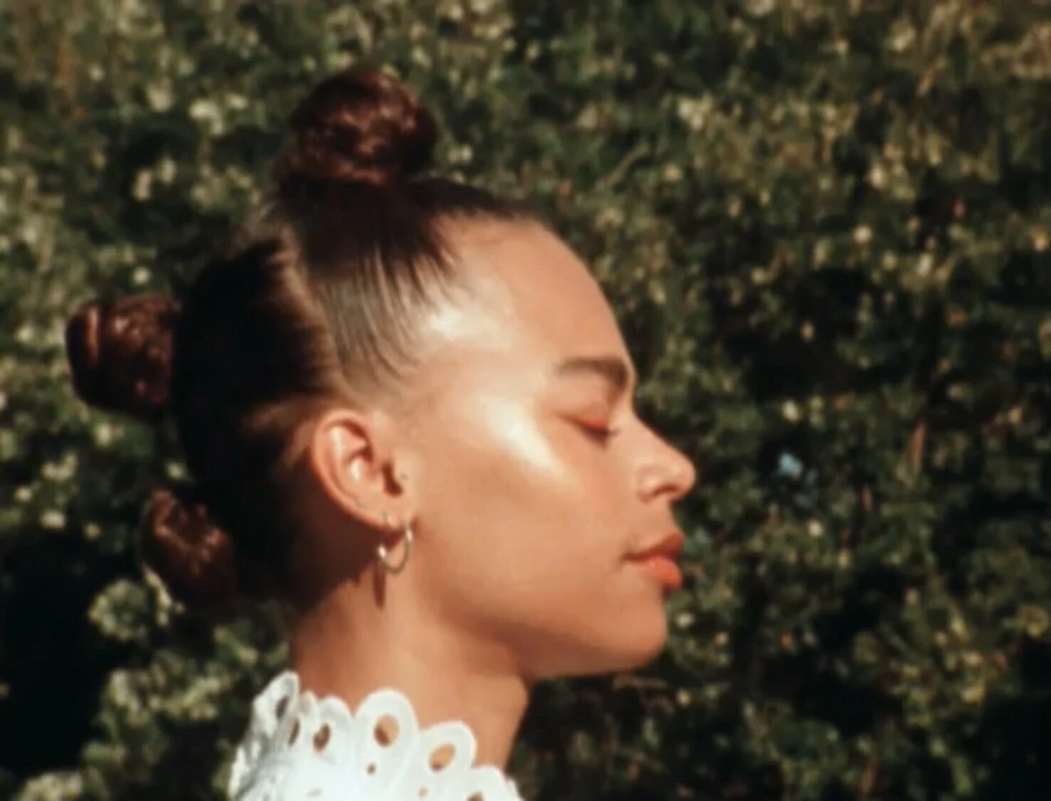 Perfil de una persona con el cabello recogido en tres moños al aire libre y con los ojos cerrados.