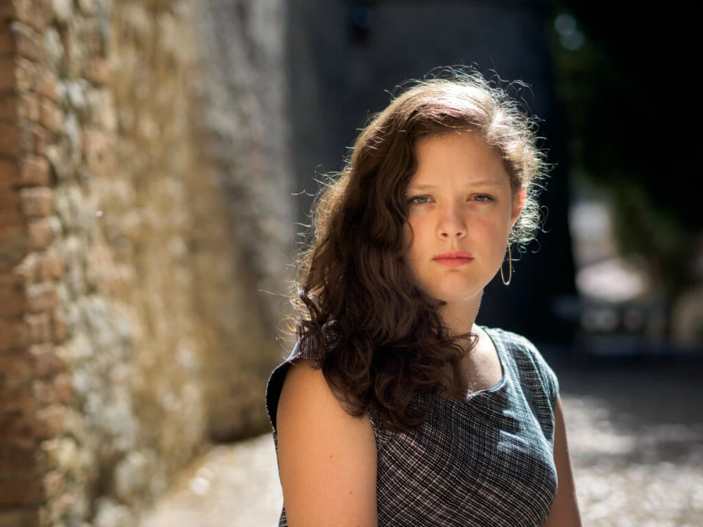 Retrato de una mujer cerca de una pared de ladrillos con el sol brillando en su cabello castaño oscuro.