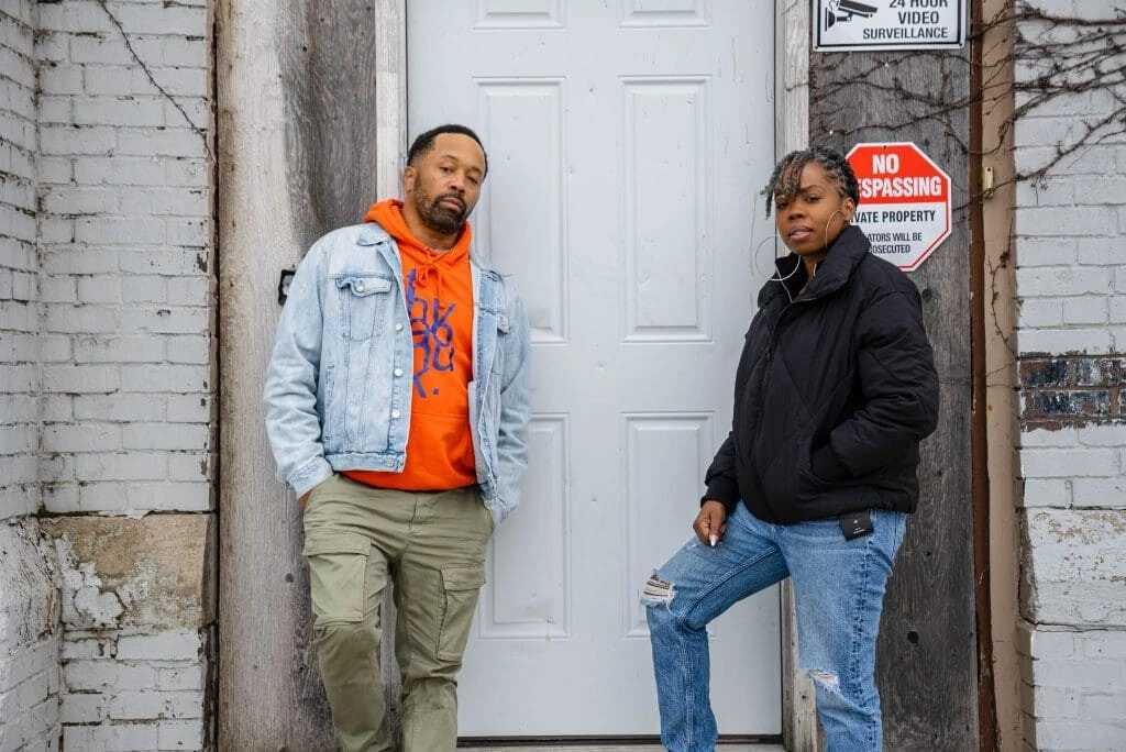 Two people stand on either side of a white exterior door dressed in cold-weather gear