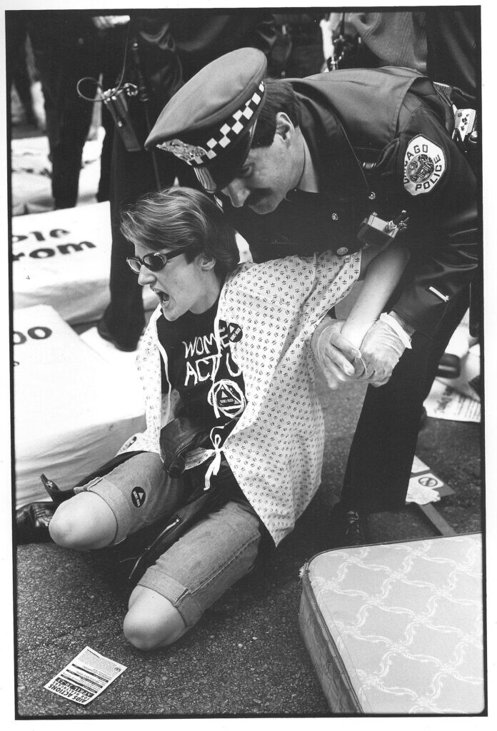 A Chicago police officer subdues a person sitting on the ground surrounded by portions of mattresses, many with text on them