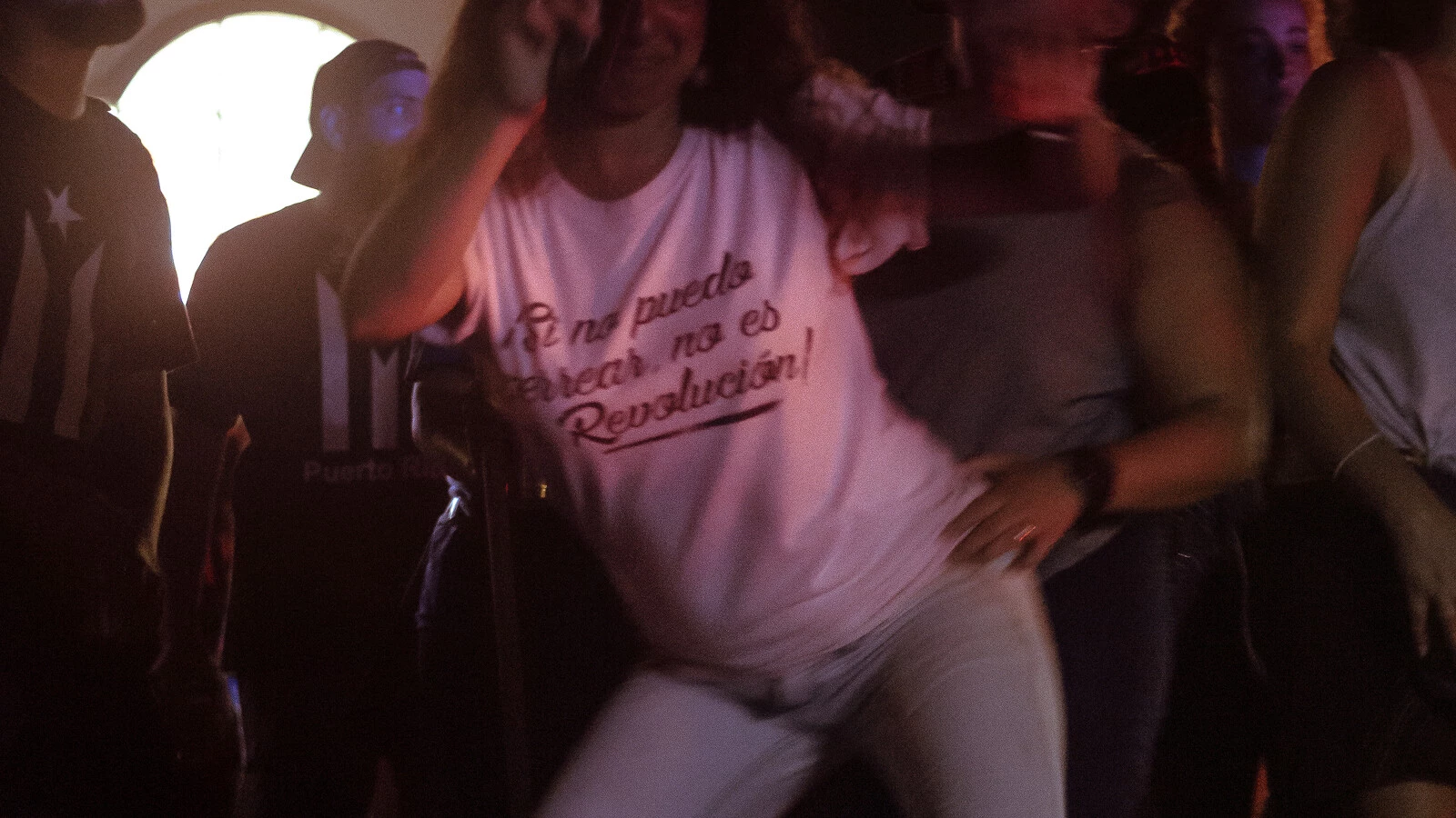 Person dancing energetically in a crowd, wearing a white t-shirt with the text 'En la muela de atrás no es revolución' (which translates to