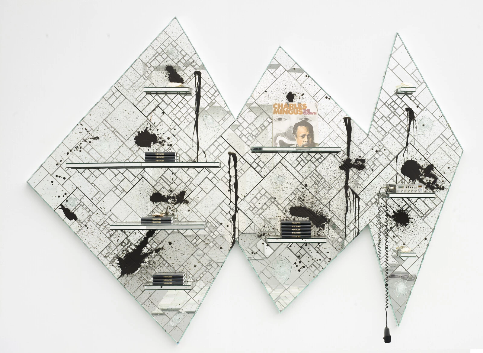 Three geometrically arranged diamond-shaped panels made up of tiled glass in various size rectangles and squares featuring shelves with piles of books on them, a Charles Mingus album, and an A-B radio. The whole thing is splattered with black.